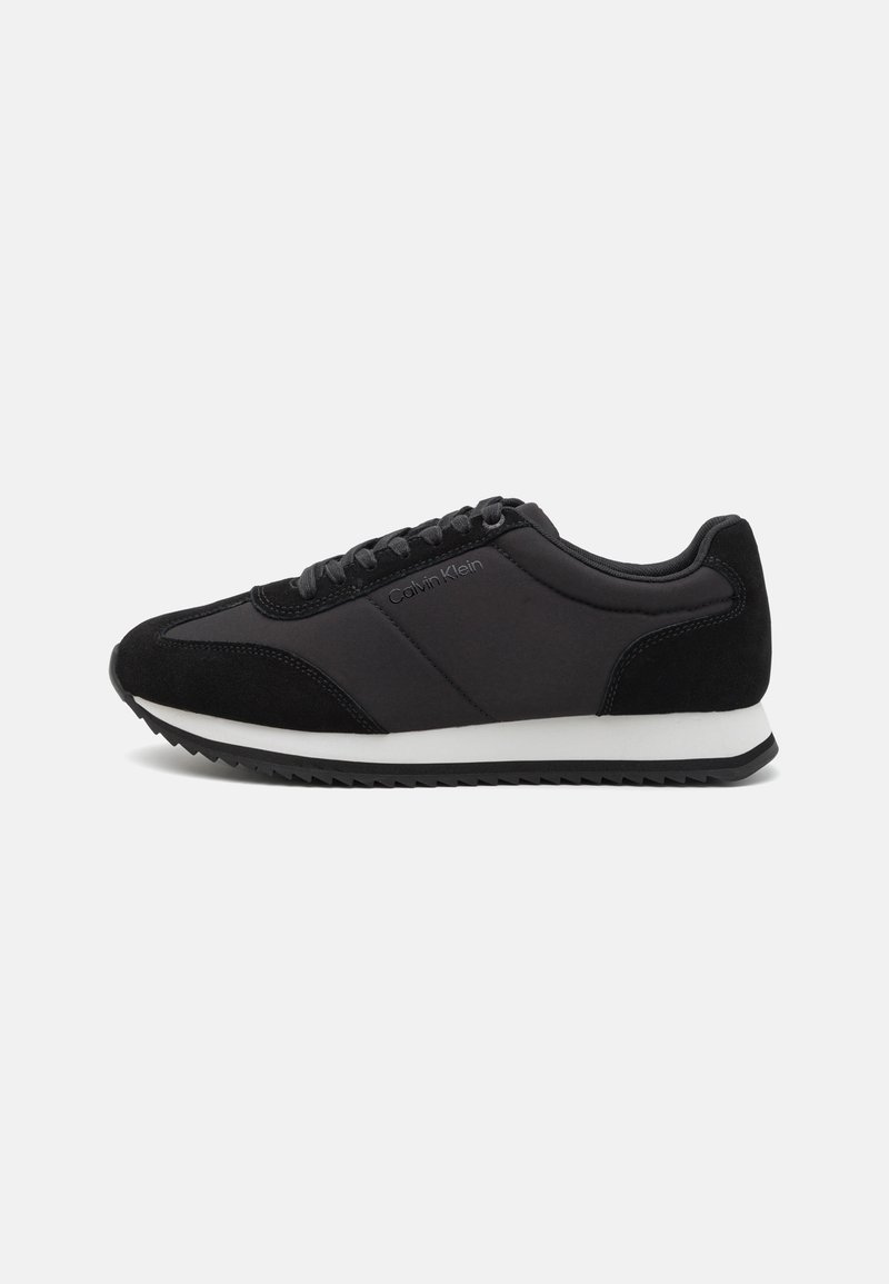 Fekete sneaker sima nylon felsőrésszel és velúr díszítéssel, fűzőkkel és fehér középtalppal. Talpa texturált tapadási mintázattal rendelkezik.