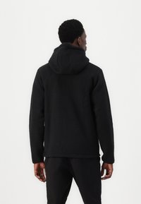 Hoodie en polaire noire avec tissu texturé, doté d'une grande capuche, de longues manches et d'une coupe décontractée, avec des coutures visibles à l'ourlet et aux poignets.