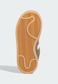 Brown suede sneaker outsole with a zigzag pattern; orange rubber grips visible; curved edges and a contrasting white side accent.