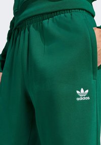 Zielone dresy wykonane z miękkiego materiału z elastycznym paskiem w talii i bocznymi kieszeniami. Na lewym udzie znajduje się białe logo Adidas.