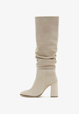 Botas beige por encima de la rodilla con parte superior arrugada, fabricadas en suave ante, con punta afilada y un tacón cuadrado grueso.