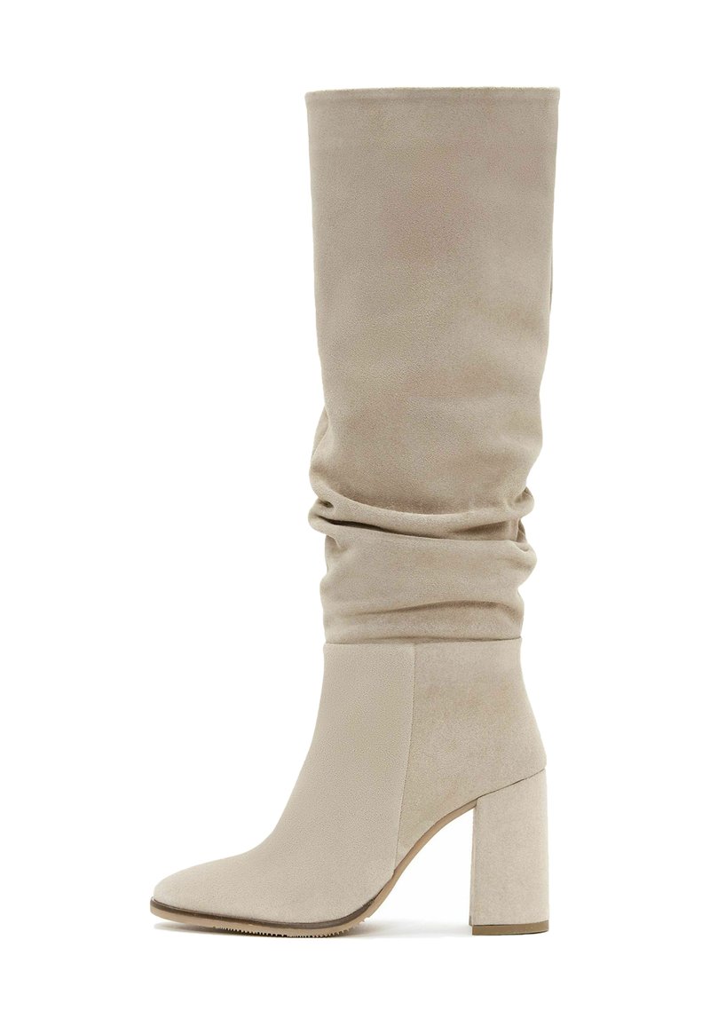 Stivali beige sopra il ginocchio con un design morbido, realizzati in suede, dotati di punta affilata e tacco largo.