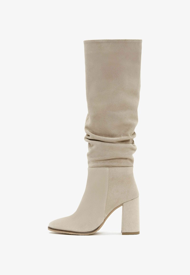 Bottes beiges au-dessus du genou avec un dessus flasque, en daim doux, présentant un bout pointu et un talon large.