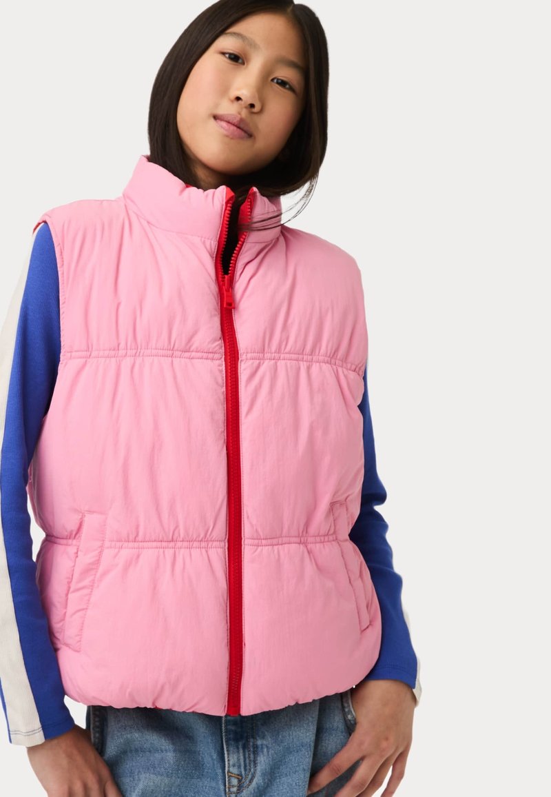Roze puffervest met hoge kraag, ritssluiting aan de voorkant en zijzakken. Gestyled over een blauwe langslieve shirt met witte accenten.