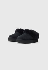 Čierne šľapky typu slip-on s hrubými štruktúrovanými podrážkami a jemným kožúškom okolo otvoru pre teplo a pohodlie.