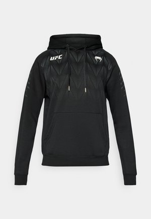 Musta huppari, jossa on geometrinen kuvio, kengurun tasku, säädettävät kiristysnauhat ja UFC-logo rinnassa. Valmistettu pehmeästä kankaasta.