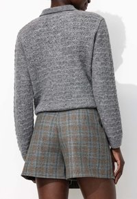 Pull en maille gris avec un motif texturé et un col, associé à un short à carreaux marron avec des lignes bleues et oranges.