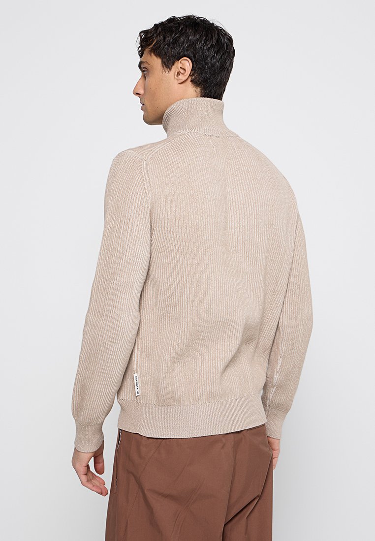Beige geripptes Rollkragensweater aus strukturiertem Strickmaterial, mit engen Bündchen und einem dezenten Logoetikett an der Seite.