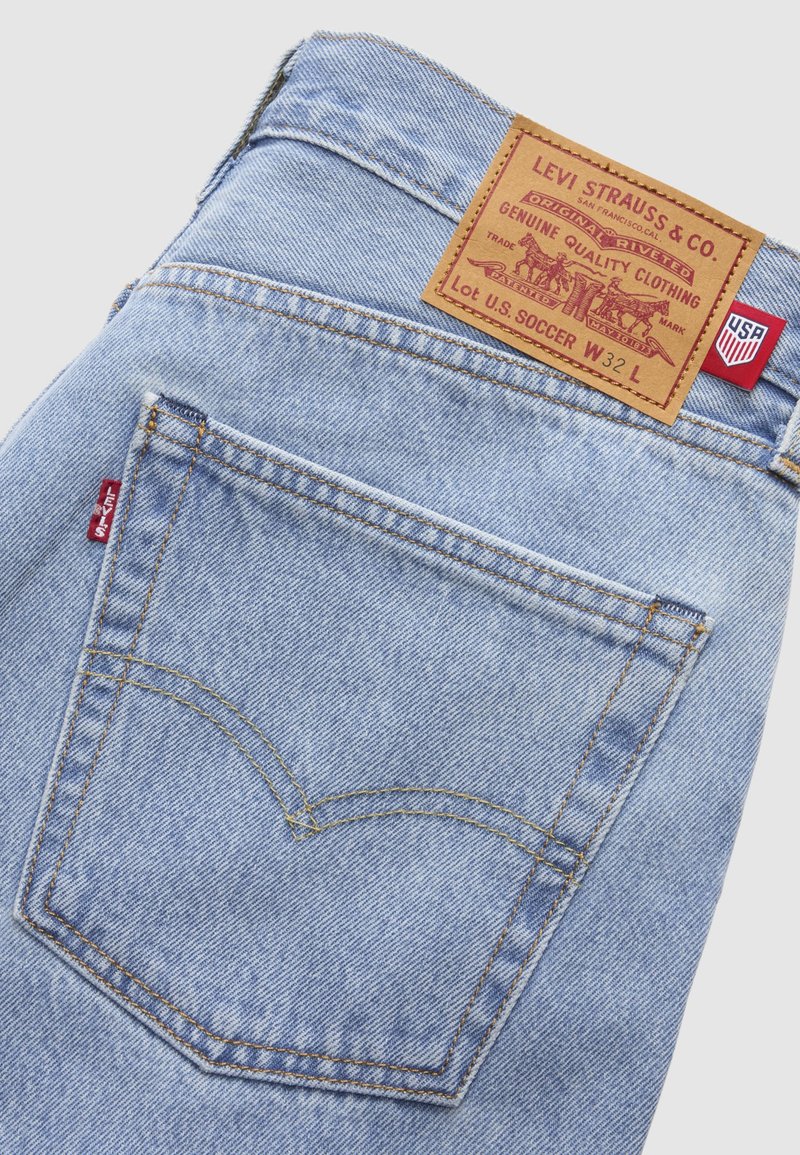 Hellblaue Levi's Jeans aus Denim mit Gesäßtasche, die das charakteristische rote Levi's Etikett und ein hellbraunes Lederpatch mit Markenlogo und Größe W32 L zeigt.