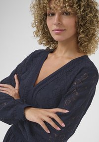 Abito blu navy a fantasia con scollatura a V profonda e maniche lunghe. Il tessuto presenta un dettaglio in pizzo testurizzato, caratterizzato da intricati disegni floreali.