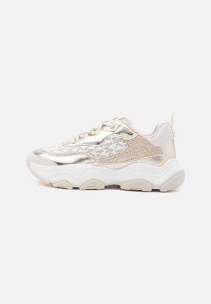 Sneaker chunky con parte superiore bianca e oro metallizzato, lati in mesh con motivo, suola bianca spessa e accenti beige su sfondo semplice.