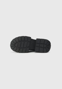 Black rubber shoe sole with a ridged pattern, featuring deep treads for traction and a wide, oval shape. Durable and flexible design.
