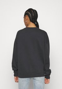 Sudadera negra de gran tamaño con mangas largas, puños y dobladillo acanalados, y un escote redondeado, exhibida desde la parte posterior sobre un fondo blanco.