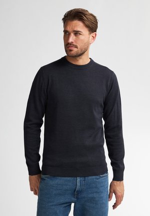 Pulover gri închis cu guler rotund dintr-un material tricotat, cu mâneci lungi și manșete cu nervuri, asortat cu blugi din denim de culoare albastru deschis.