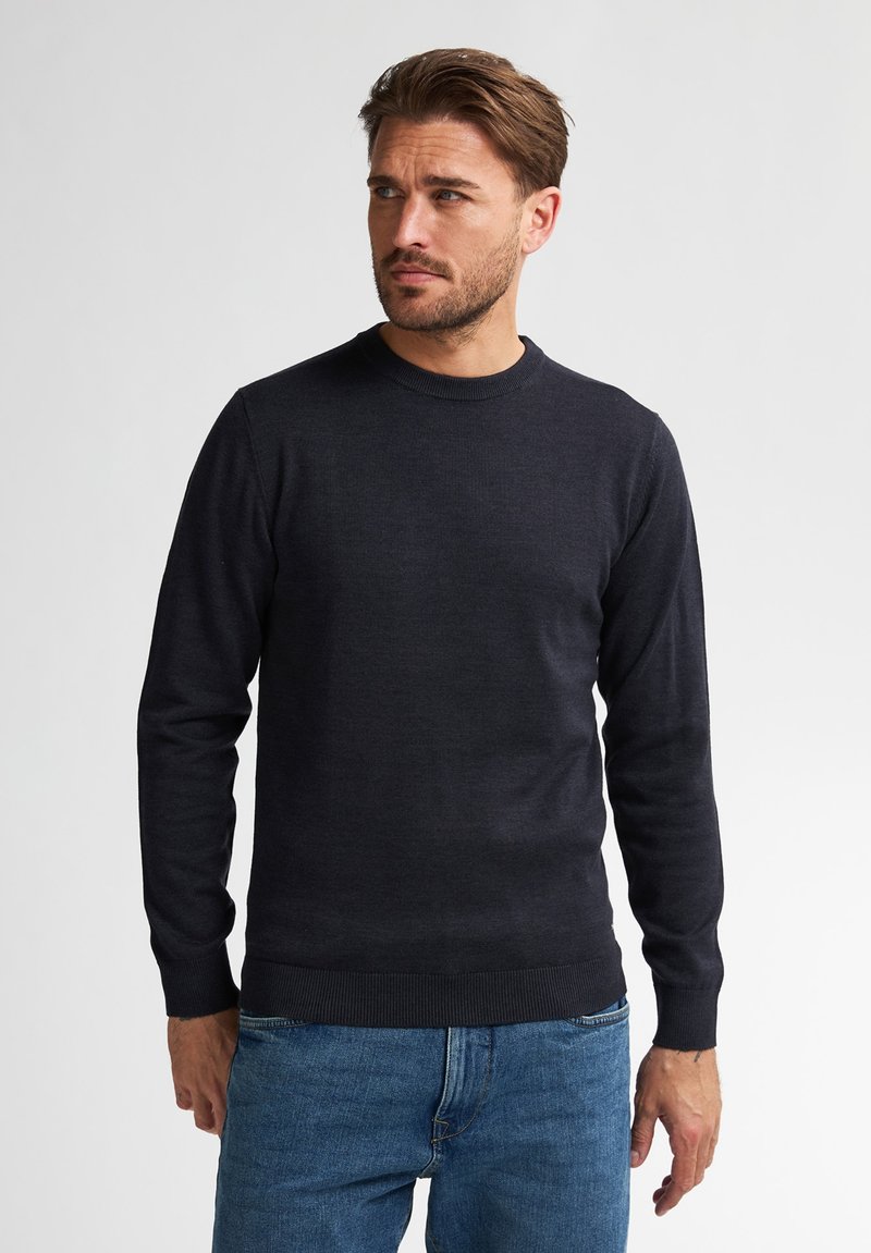 Ciemnoszary sweter z okrągłym dekoltem, wykonany z dzianiny, z długimi rękawami i ściągaczami, w zestawie z jasnoniebieskimi dżinsami.