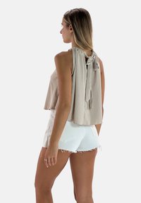 Top beige senza maniche con dettaglio del nodo sul retro e tessuto fluido, abbinato a pantaloni corti bianchi con orli sfilacciati. Texture morbida, vestibilità rilassata.