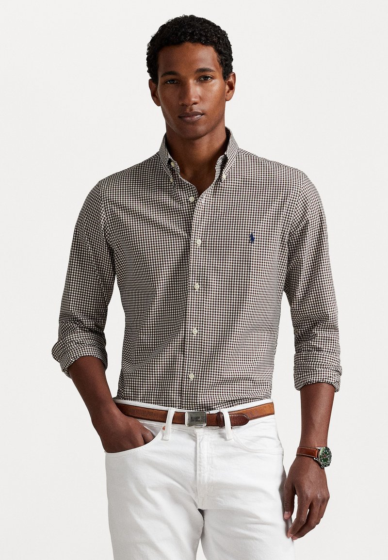 Brown and white checked button-down shirt with a collar, paired with white pants and a brown belt. Watch with a green face is worn on the wrist.