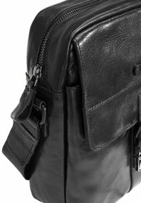 Czarna skórzana torba na ramię z zamkiem błyskawicznym, przednią kieszenią na klapę i regulowanym paskiem. Charakteryzuje się gładką teksturą i minimalistycznymi akcentami metallicznymi.