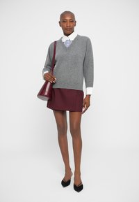 Grauer Wollpullover mit V-Ausschnitt über einem weiß-karierten, blau gestreiften Hemd, kombiniert mit einem bordeauxfarbenen Minirock und einer kastanienbraunen Handtasche.