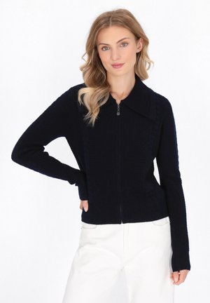 Marineblaue Zip-Up-Strickjacke mit ribbeliger Textur, großem Kragen und langen Ärmeln, entworfen mit seitlichen Einsätzen für eine strukturierte Passform.