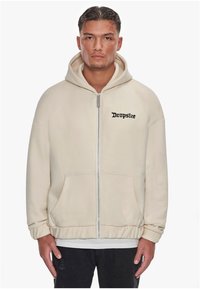 Creme zip-up hoodie med en frontlomme, ribbede manchetter og broderet "Dropsize" logo i sort på brystet. Blødt, tekstureret stof.