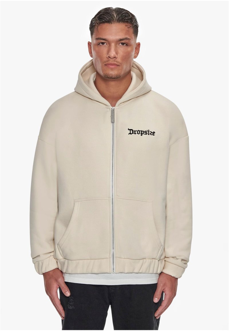 Creme zip-up hoodie med en frontlomme, ribbede manchetter og broderet "Dropsize" logo i sort på brystet. Blødt, tekstureret stof.