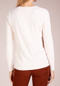 Långärmad, ljusrosa bomullstopp med rundad halsringning och en slät yta, tillsammans med rödbruna manchesterbyxor med bakfickor.