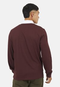 Polo a maniche lunghe borgogna con colletto bianco, caratterizzato da una vestibilità comoda e una texture morbida. La vista posteriore mostra un design semplice e dettagli minimi.