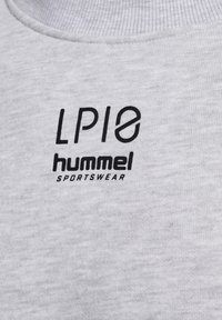 Gros plan sur un tissu gris avec le logo noir « LP10 hummel SPORTSWEAR » imprimé près du col d'un vêtement.
