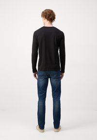 Sort langærmet skjorte, blå slim-fit jeans med let slidte detaljer. Casual stil, blødt stof og enkelt design. Lyse sko.