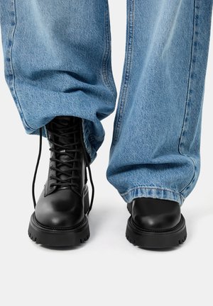 Black lace-up boots with a rounded toe, thick rubber sole, paired with loose light blue denim jeans.