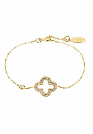 Delicate gold chain bracelet with a clover-shaped pendant outlined with small clear gemstones and a gold clasp with a small tag.