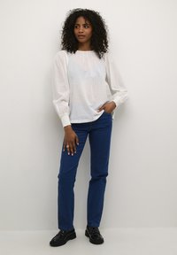 Vit blus med prickar och pösiga ärmar med elastiska manschetter, tillsammans med blå raka jeans och svarta lackläderskor.