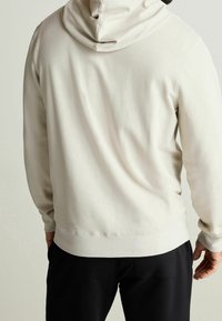 Mikina s kapucí v světle béžové texturované látce. Má přiléhavý spodní lem a manžety. Hladký vnitřek, ležérní design, vhodná k vrstvení.