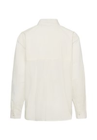 Chemise blanche à manches longues vue de dos avec un col classique et des poignets boutonnés sur un fond uni.