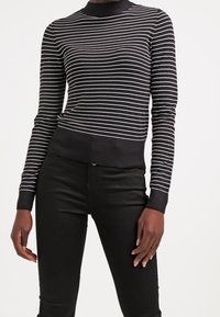 Musta-valkoraidallinen neulepaita korkealla kaula-aukolla ja resorilla helmassa, neulottua kangasta; istuva malli, jossa pitkät hihat.