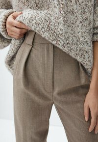 Pull en tricot avec un motif texturé gris clair et marron, associé à un pantalon beige taille haute avec plis et poches latérales.