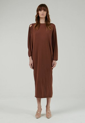 Vestido midi marrón de manga larga con corte off-shoulder, textura suave y un ajuste relajado, combinado con zapatos de tacón transparente.