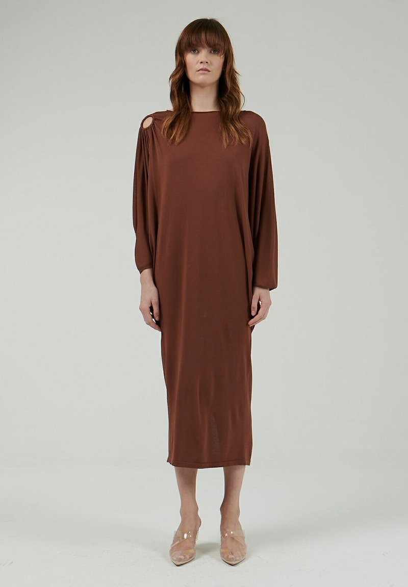 Vestido midi marrón de manga larga con corte off-shoulder, textura suave y un ajuste relajado, combinado con zapatos de tacón transparente.