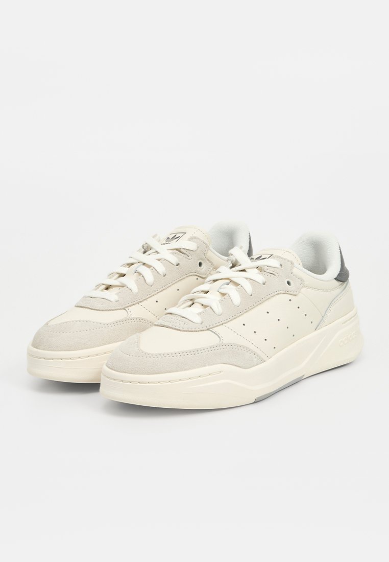 Baskets de sport beige clair en cuir lisse et en daim, dotées de perforations sur les côtés et d'un subtil accent gris au niveau du talon.