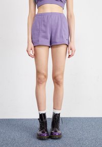 Shorts in cotone viola con vita elastica, dotati di una tasca laterale e di un piccolo logo nero. Abbinati a stivali da combattimento neri e viola.