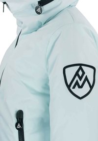 Veste bleu clair avec une finition lisse et brillante, un logo noir brodé sur la manche et des accents zippés noirs.