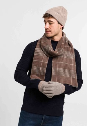 Beige strikket hue, brunt ternet tørklæde, grå handsker, marineblå ribbet sweater, der viser teksturdetaljer og farvekontrast.