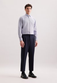 Camicia a quadri azzurro chiaro con colletto button-down, abbinata a pantaloni blu scuro e scarpe nere. Linee pulite e vestibilità su misura.