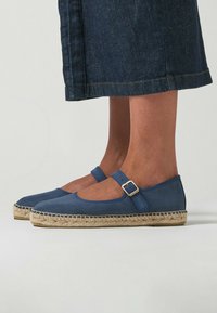 Espadrilles de lona azul con punta redonda, correa en el tobillo y hebilla, entresuela de yute y suela plana, combinadas con una falda de mezclilla oscura.