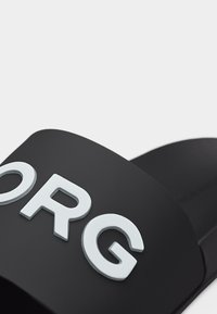 Μαύρο υποδήμα σαγιονάρας από λάστιχο με μεγάλα λευκά ανάγλυφα γράμματα που σχηματίζουν το "ORG" στο λουράκι.