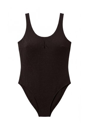Femme debout pieds nus vêtue d’un maillot de bain une pièce noir sans manches avec un logo discret sur la poitrine sur un fond gris uni.