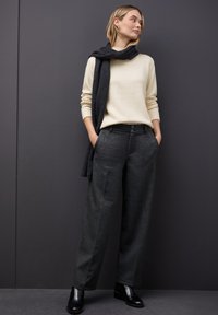 Pantalon large gris, pull en tricot crème et écharpe noire. Bottines noires. Texture lisse, coupe ajustée et détails de design subtils.