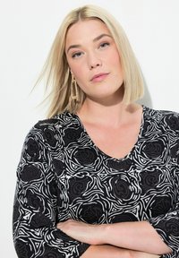 Schwarz-weiß gemusterte Bluse mit V-Ausschnitt und Dreiviertelärmeln. Besitzt wirbelnde Blumendesigns und eine weiche, strukturierte Oberfläche.