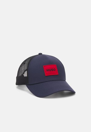 Marinehætte med en rød rektangulær lap mærket "HUGO." Har en solid front og net-sider for åndbarhed. Buet skygge design.